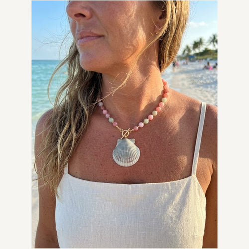 Eos necklace of pastel pink, peach and green chalcedony beads with a sealed scallop shell pendant, worn on the beach