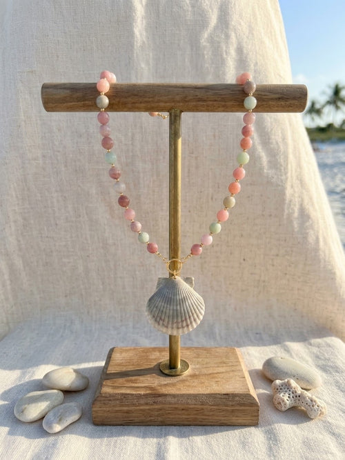 Eos necklace hanging on a wooden T-stand with beach stones and coral