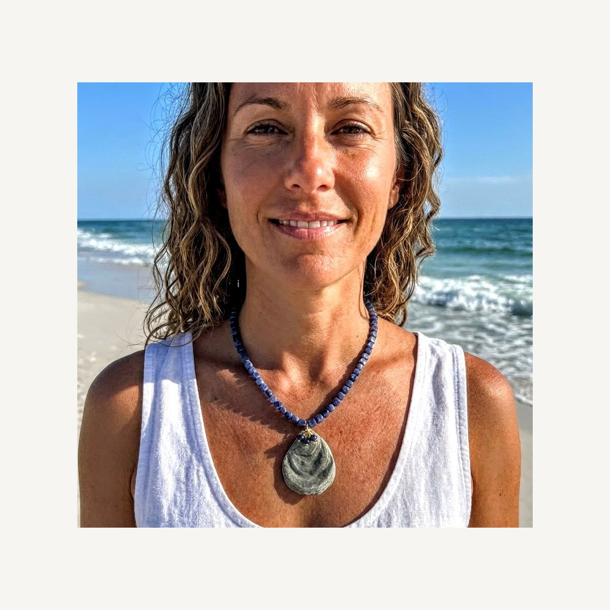 Thetis necklace of dark blue sodalite cubes with a grey oyster shell pendant, worn on the beach
