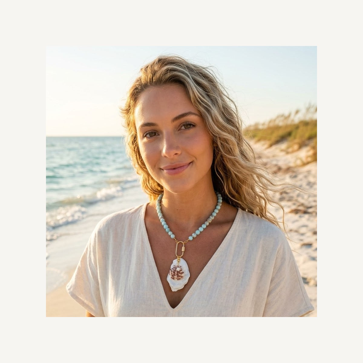 Galatea necklace of aqua beads with a white oyster shell pendant, worn on the beach