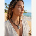 Glauce necklace worn by Jeni on the beach: dark green stone beads with an oyster shell pendant