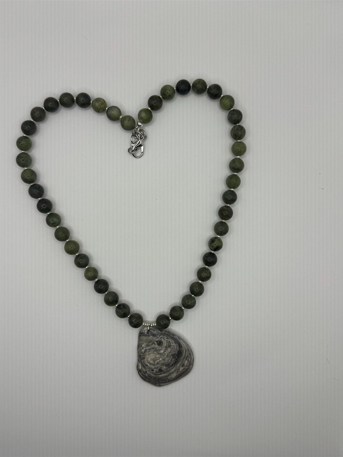 Glauce necklace laid flat in a heart shape: dark green stone beads, silver spacers and an oyster shell pendant