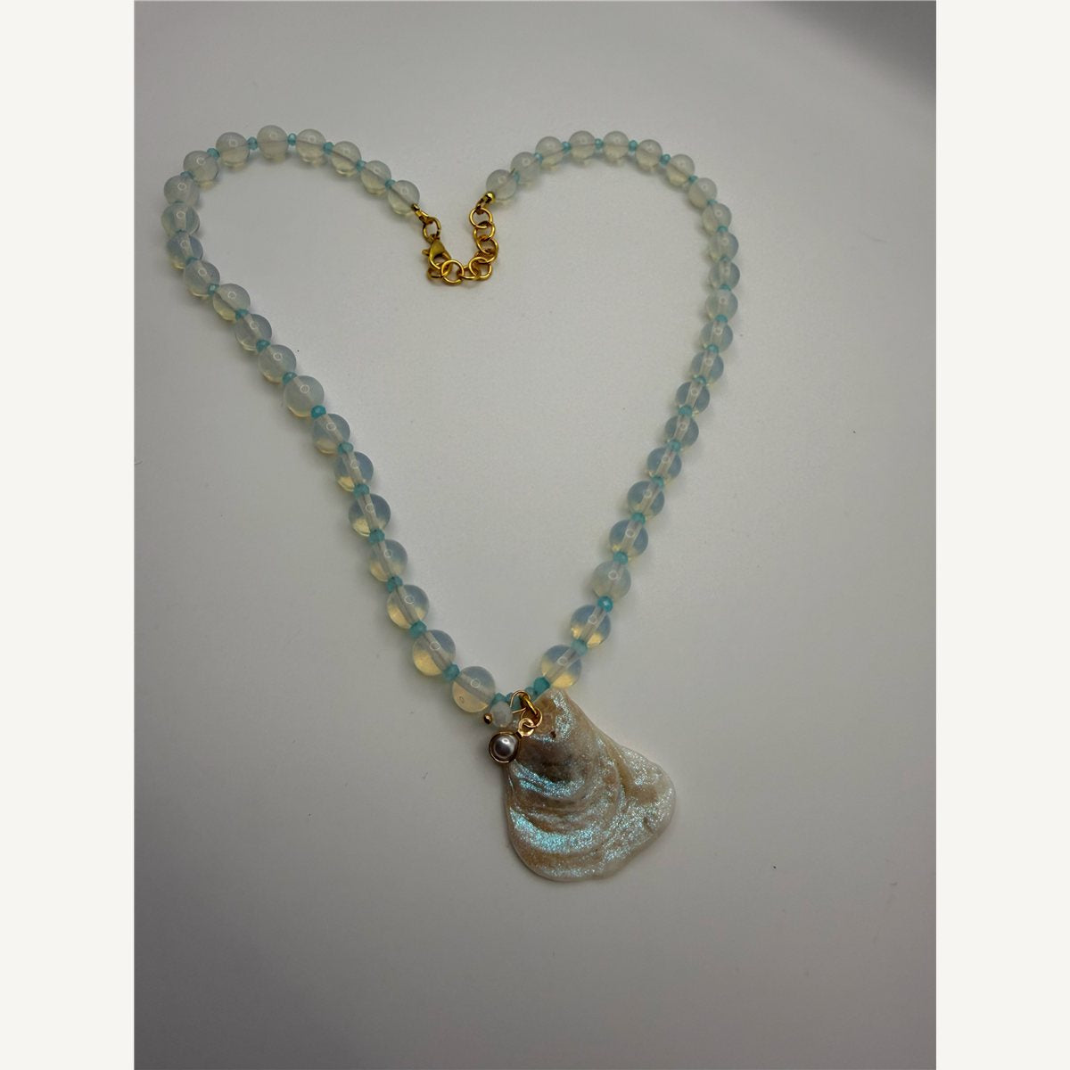 Selene necklace laid in a heart shape: white moonstone beads with aqua spacers, a pearl charm and a shimmery oyster shell pendant